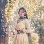 Portrait of a woman in traditional South Asian attire standing outdoors under trees.